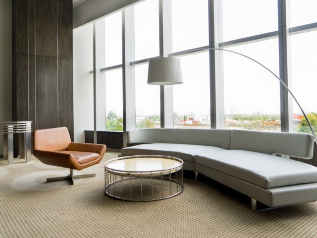 Modern lounge room interior in office building. Room with panoramic window, modern leather chair, white sofa and floor lamp. Downtown workspace design concept